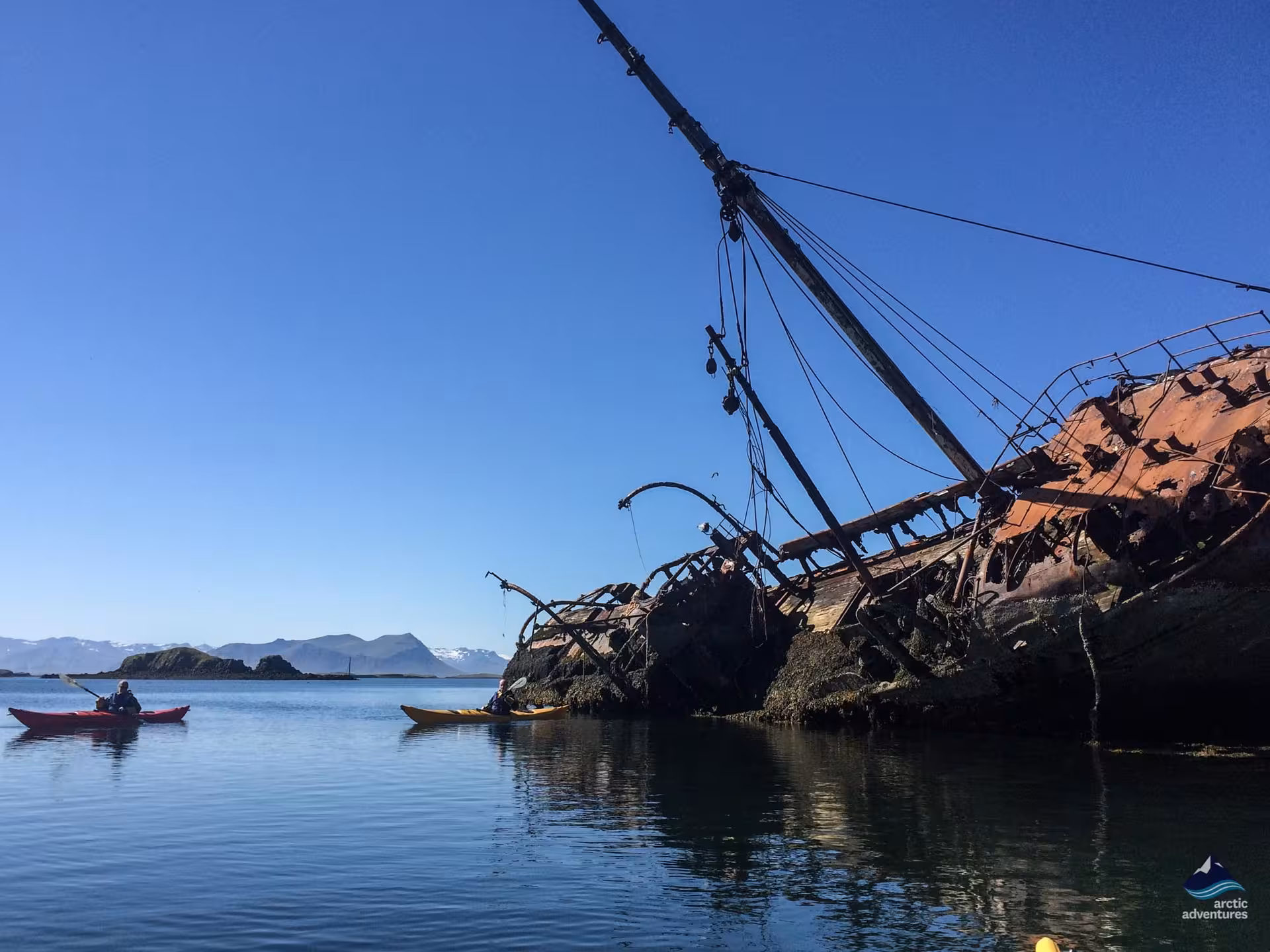 Kayakers paddle by the Garðar BA 64 shipwreck in the Westfjords, Iceland, on a private coastal adventure