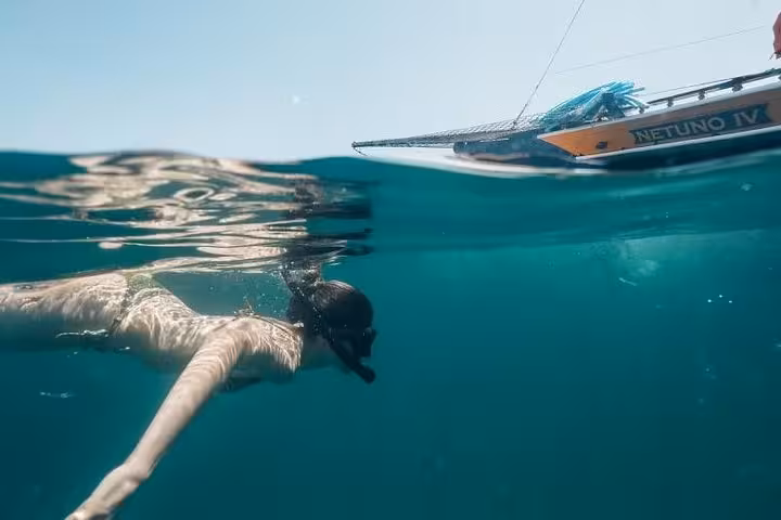Snorkeler enjoying a vibrant underwater view beside a traditional boat during a scenic boat tour experience.
