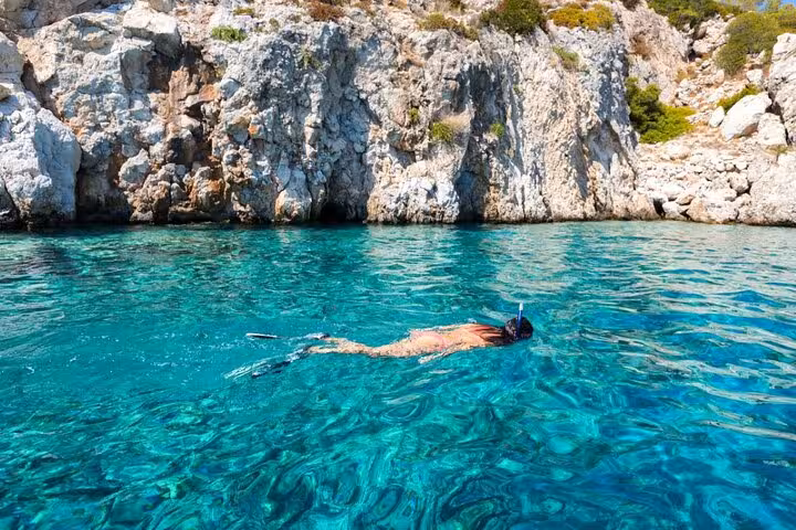 Snorkeler in crystal-clear Paleokastritsa waters by rocky cliffs on a private Corfu beaches tour