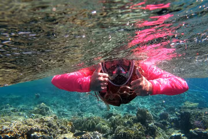 Snorkeler in full-face mask giving thumbs up above Ras Mohamed coral reef on White Island snorkeling trip from Sharm