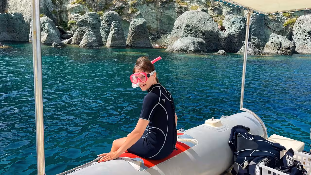 A snorkeler in a wetsuit enjoys the serene waters of Capo Marrargiu, Bosa, from a boat near rocky shores.