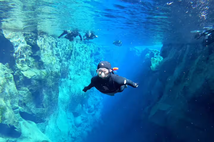 Snorkeler in wetsuit explores the clear waters of Silfra fissure in Iceland, showcasing vibrant underwater landscapes.