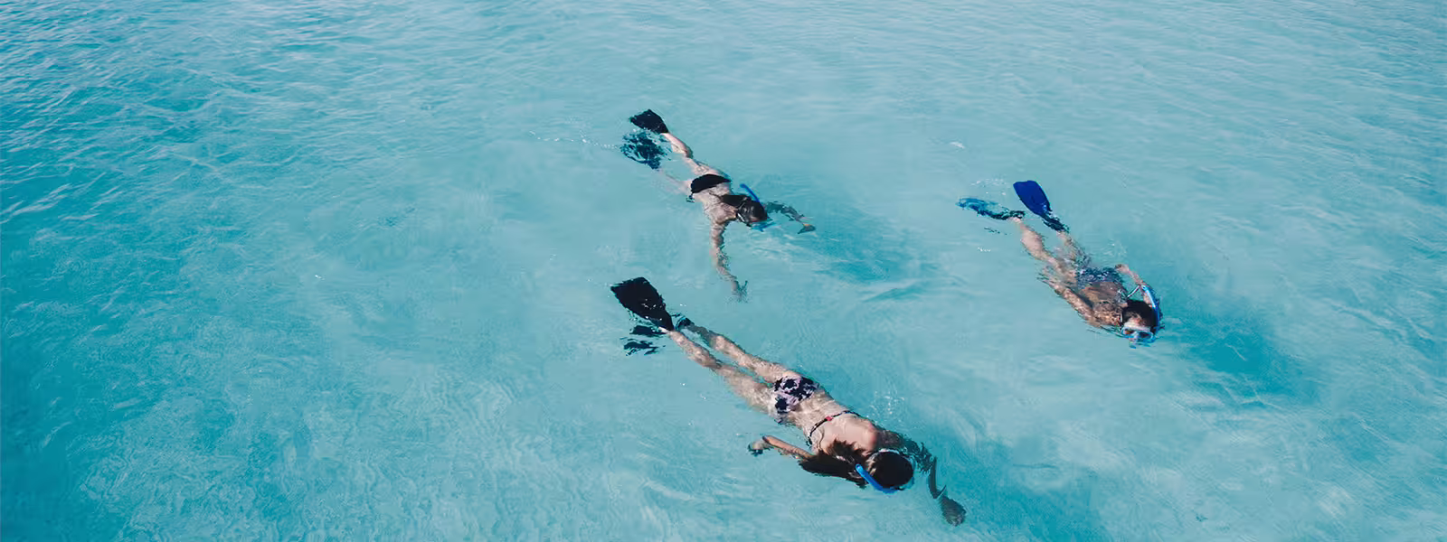 Three snorkelers exploring vibrant blue waters on a Costa Brava snorkeling trip.