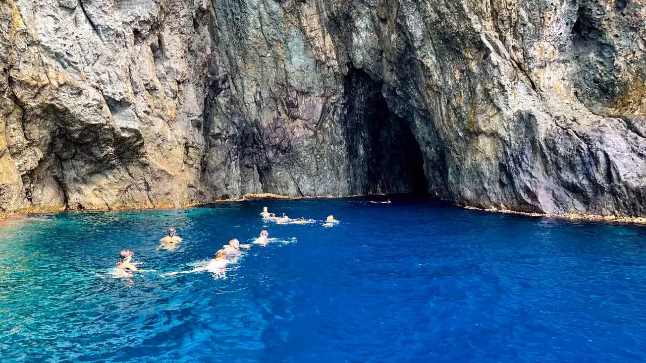 Group of snorkelers swimming near a dramatic sea cave in the deep blue waters of Capo Marrargiu, Bosa.