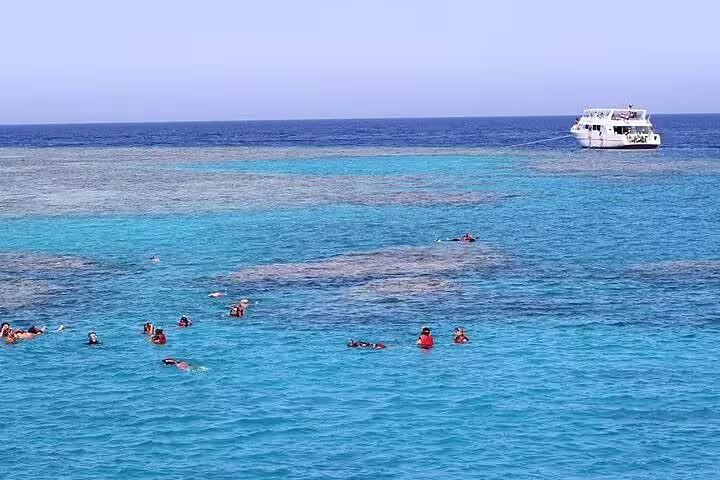 Snorkelers in turquoise Marsa Mubarak lagoon, Marsa Alam Red Sea, with tour boat during dugong trip