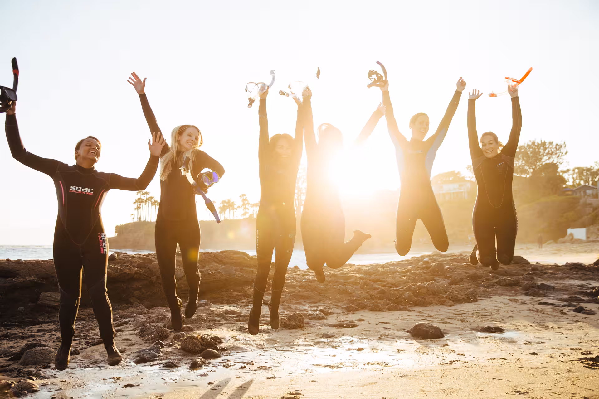 Group of excited snorkelers jumping on a sunny beach in Dubai, ready for their snorkeling adventure to Fujairah.
