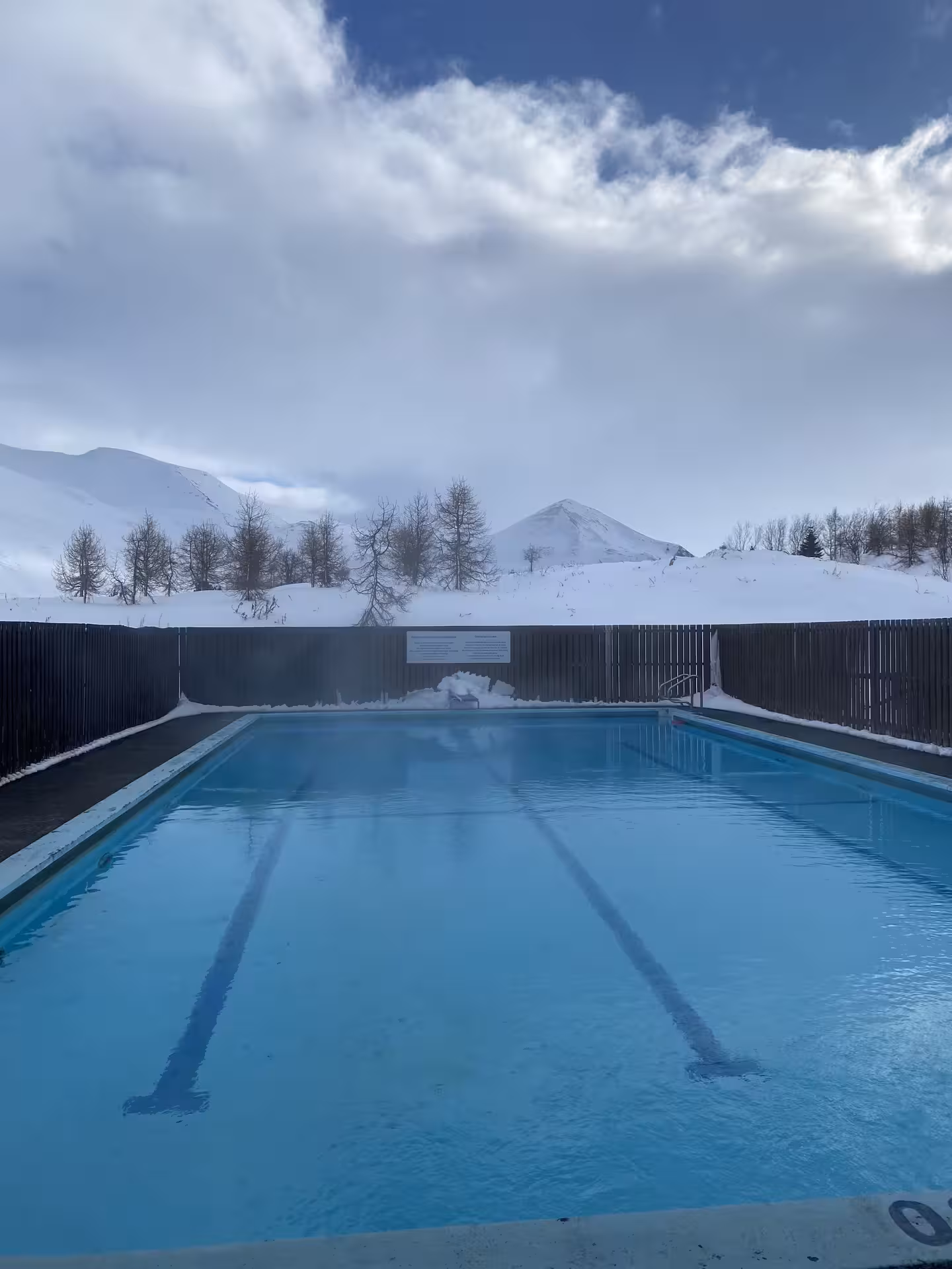 Outdoor geothermal pool after snowshoeing in Fljótin, Iceland, with snowy peaks and steam under winter sky