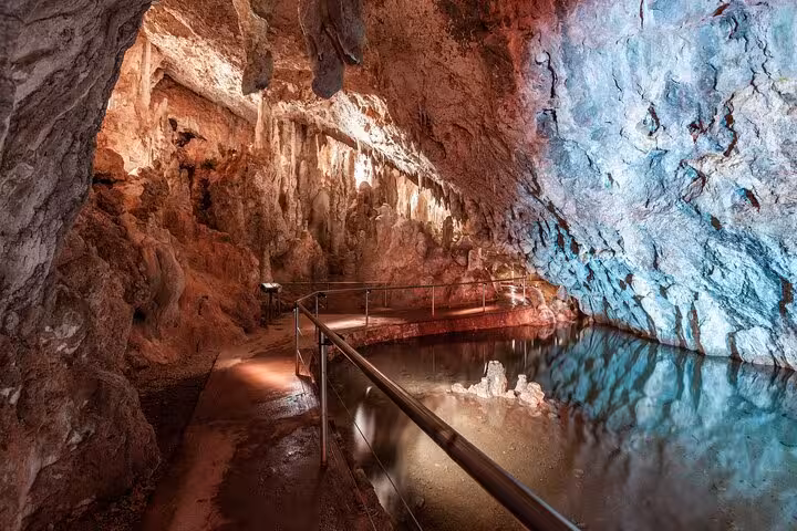 Enchanting illuminated cave with stalactites and reflective water, a highlight of the Snowy Mountains NSW tour.