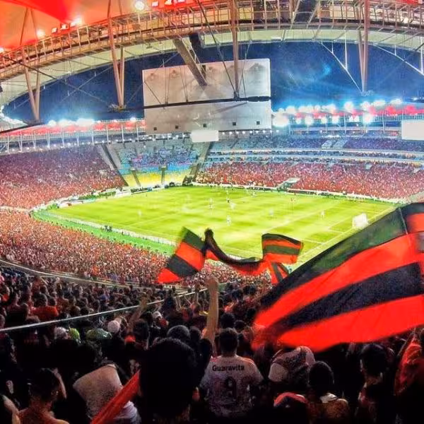 Excited fans with flags at a thrilling soccer game in Maracanã Stadium, Rio de Janeiro, under illuminated roof.