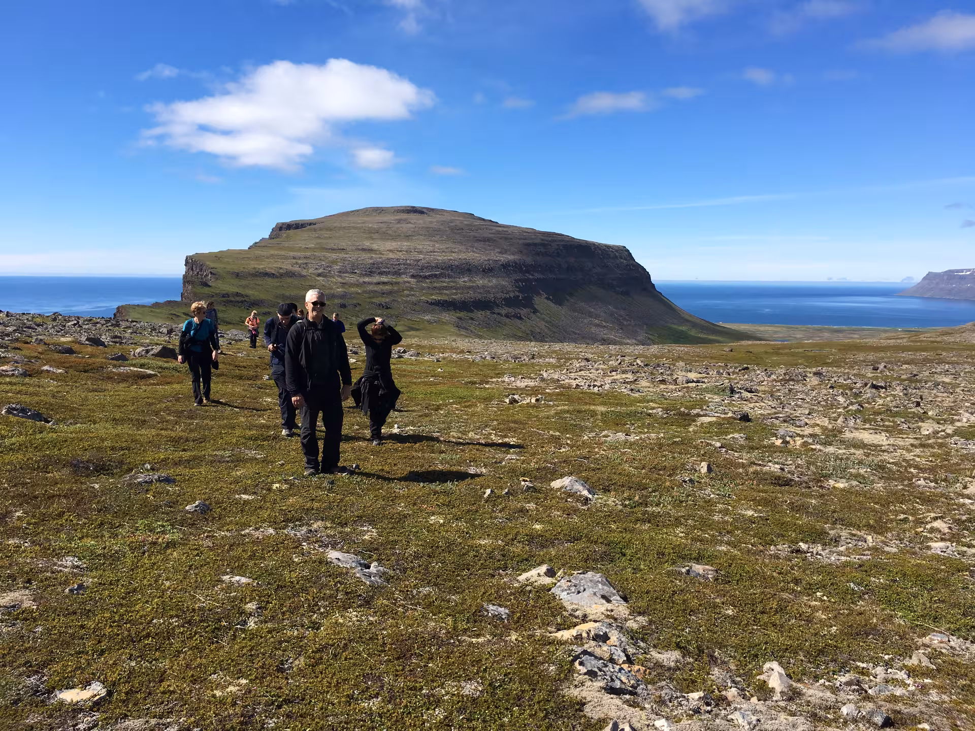 Guided hikers cross tundra with ocean and mountain views, ideal Solar Eclipse Hike trail in the Arctic