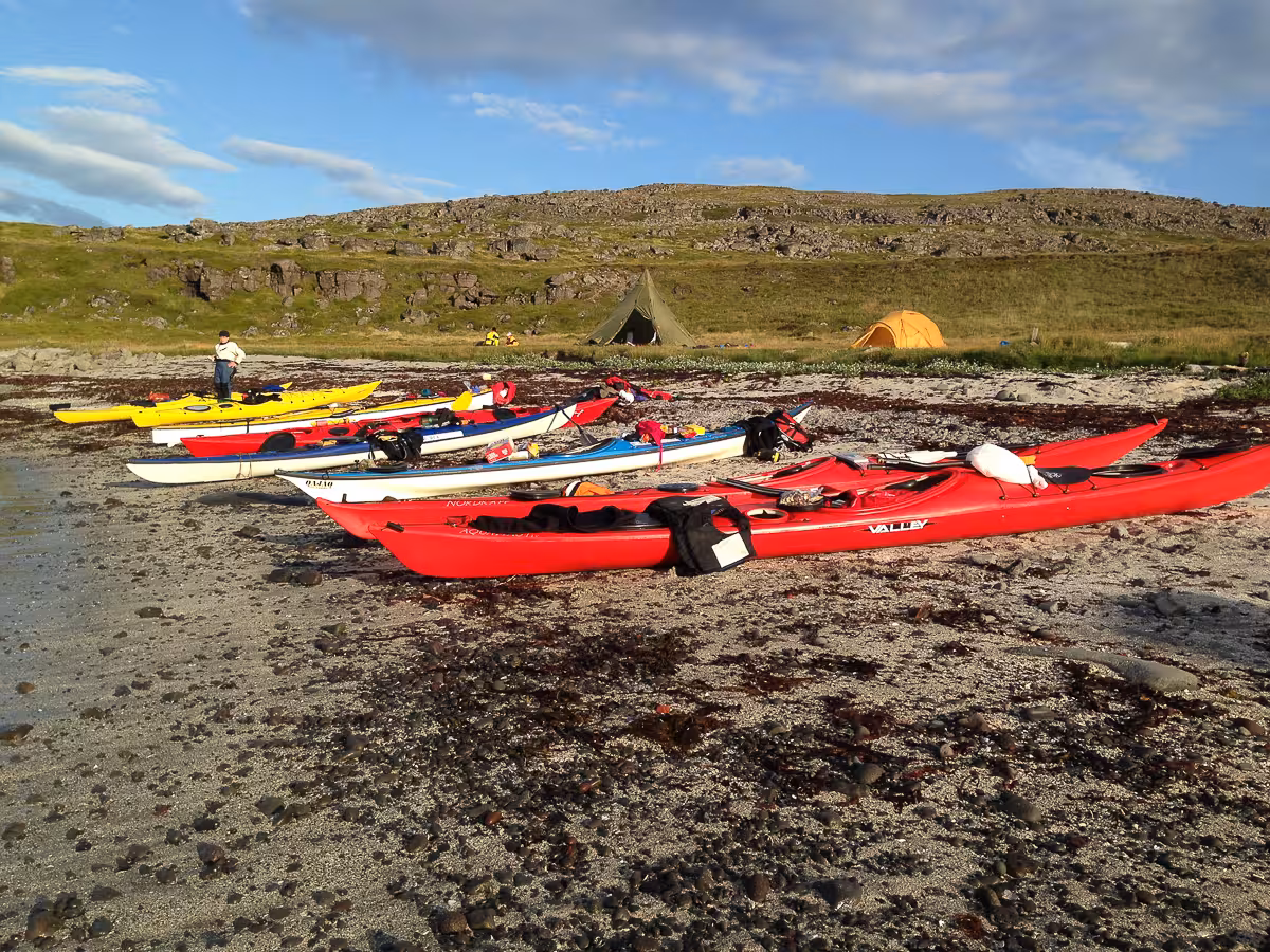 Kayaks lined on a remote beach beside tents at basecamp on the Solar Eclipse Wild Camp Discovery adventure