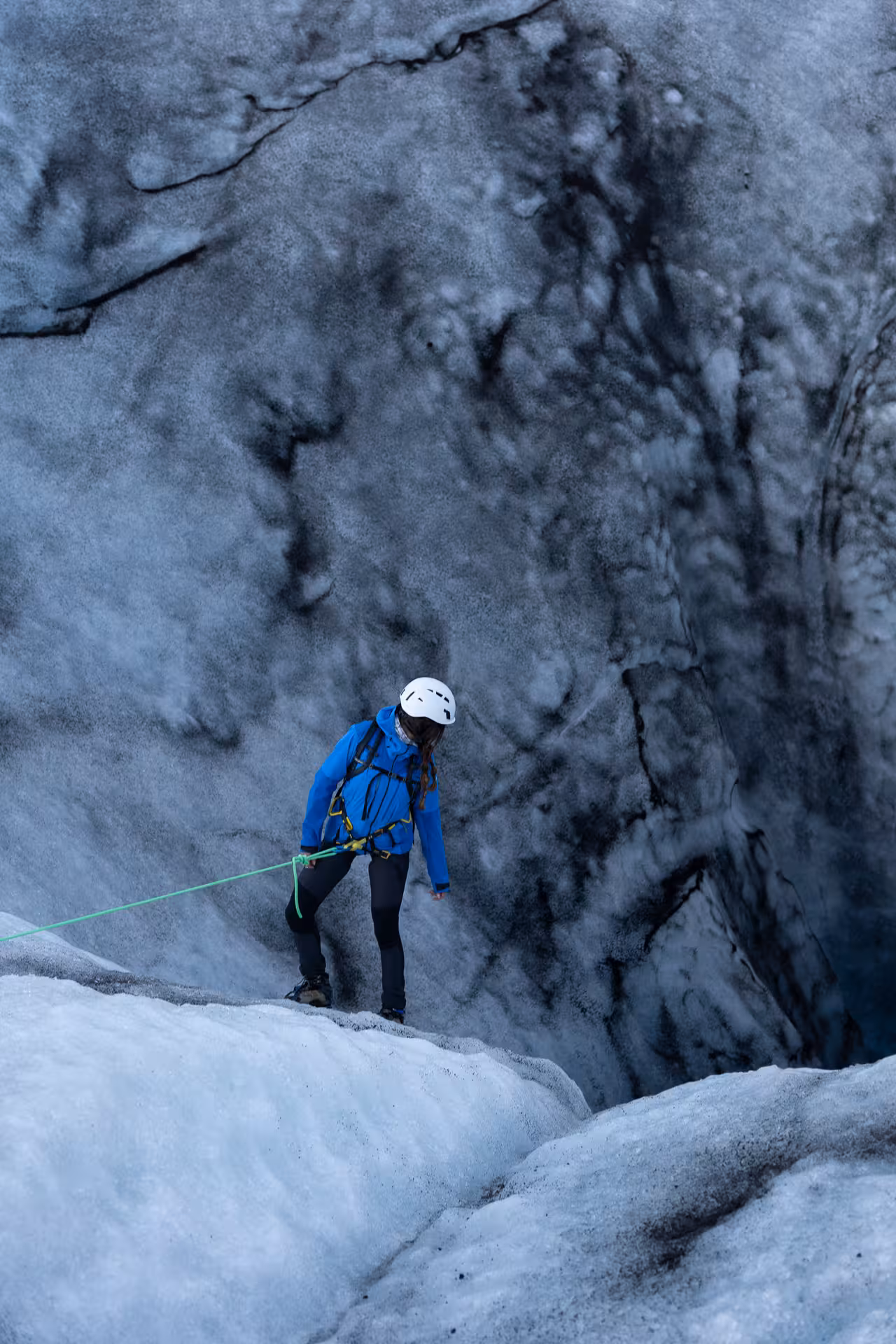 Roped hiker in helmet and blue jacket descending icy crevasse on Sólheimajökull glacier hike, Iceland