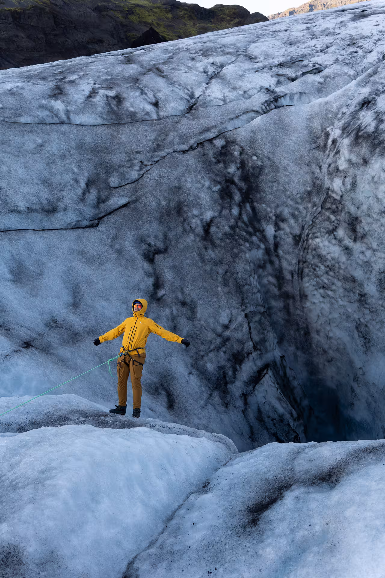 Hiker in yellow jacket on Sólheimajökull glacier near deep crevasse, guided glacier hike in Iceland