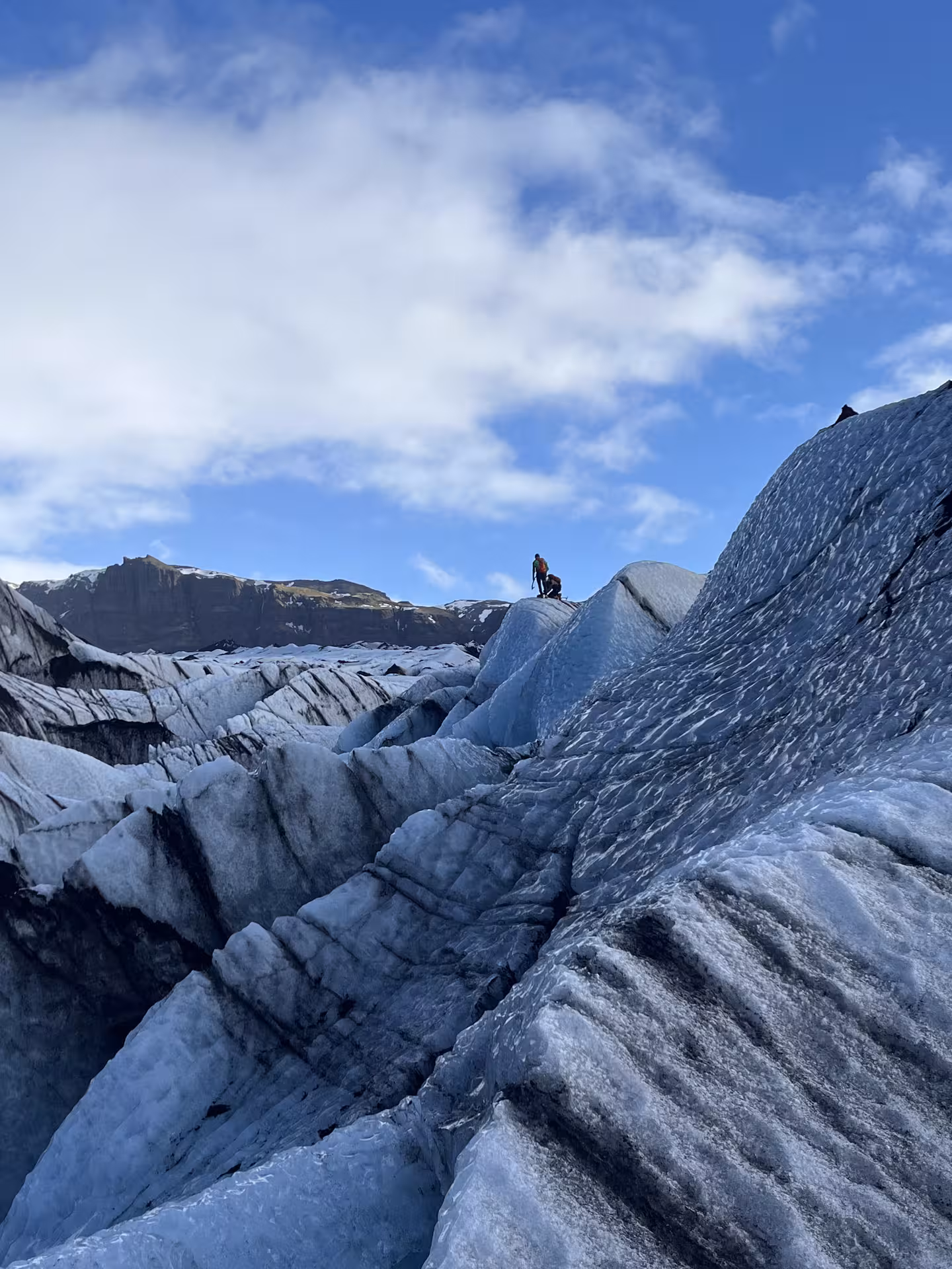 Hikers traverse rugged blue ice ridges on Sólheimajökull glacier hike and ice climbing tour in Iceland