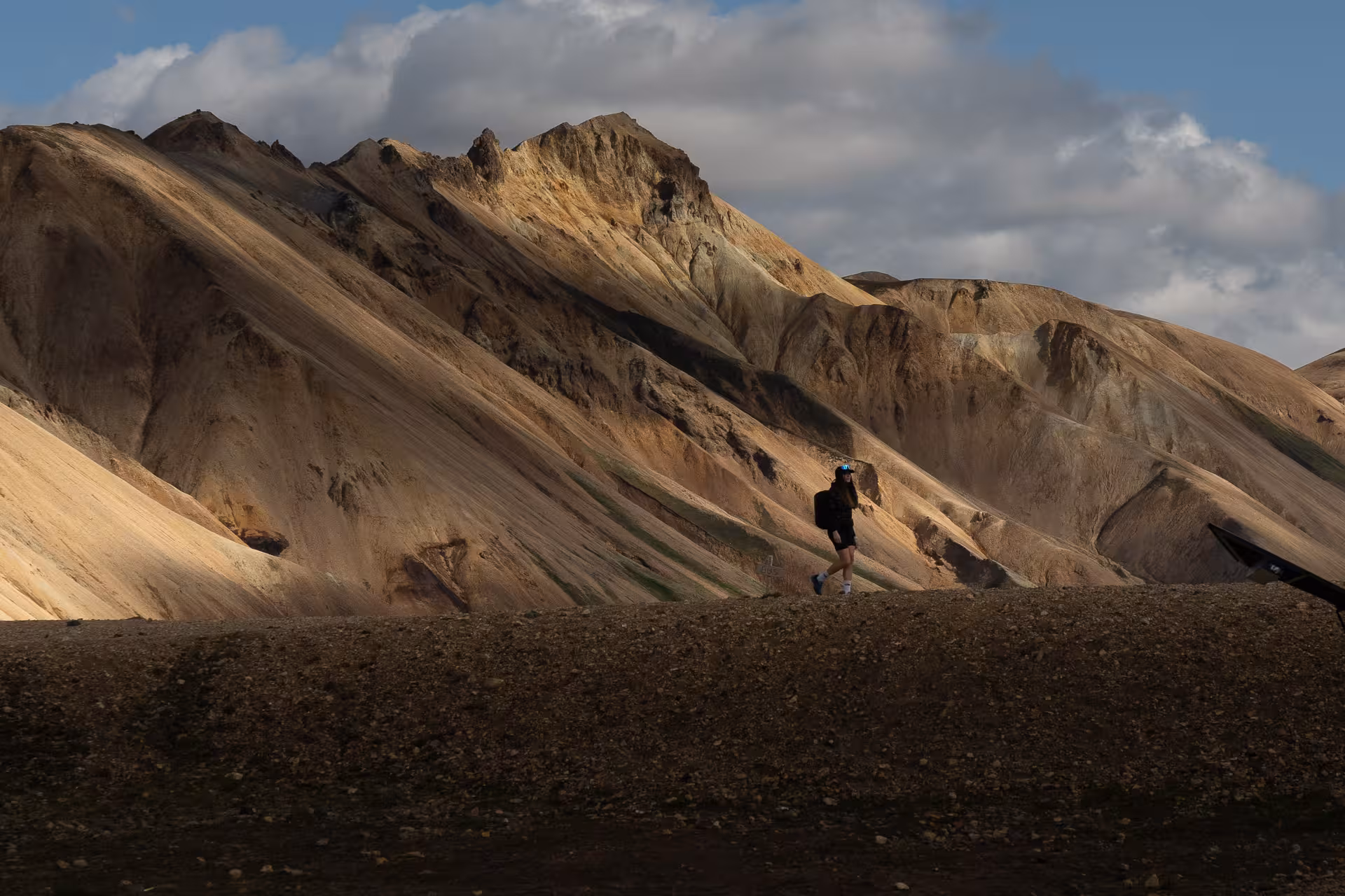 Solo hiker walking below colorful rhyolite mountains in Landmannalaugar, Iceland Highlands hiking tour view