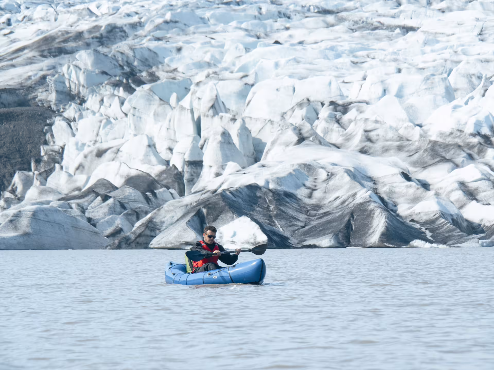 Solo packrafter paddling a calm glacier lagoon near blue ice formations on an Intro to Glacier Packrafting tour