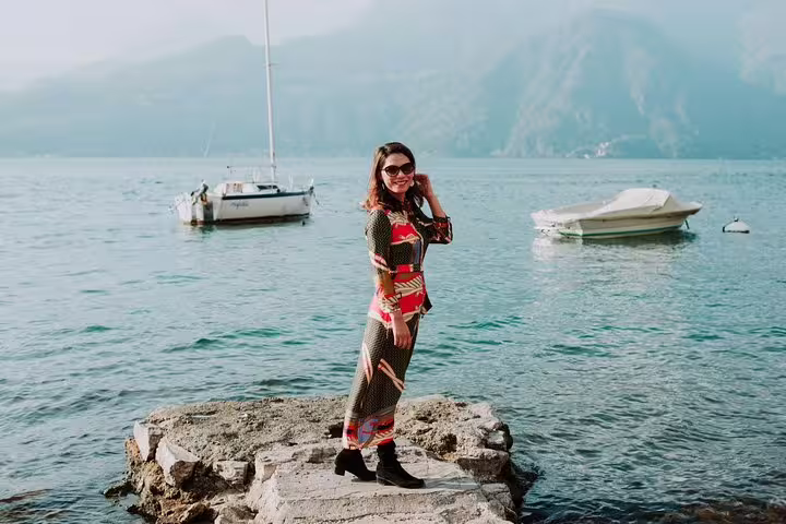 Solo traveler posing on lakeside rocks in Lake Como with boats, shot by personal travel photographer