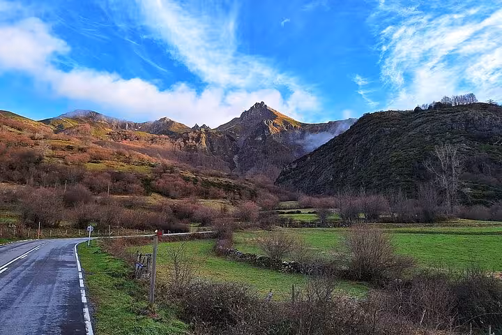 Idyllic road leading through lush green fields and mountains under a vibrant blue sky in Somiedo Natural Park, Asturias.