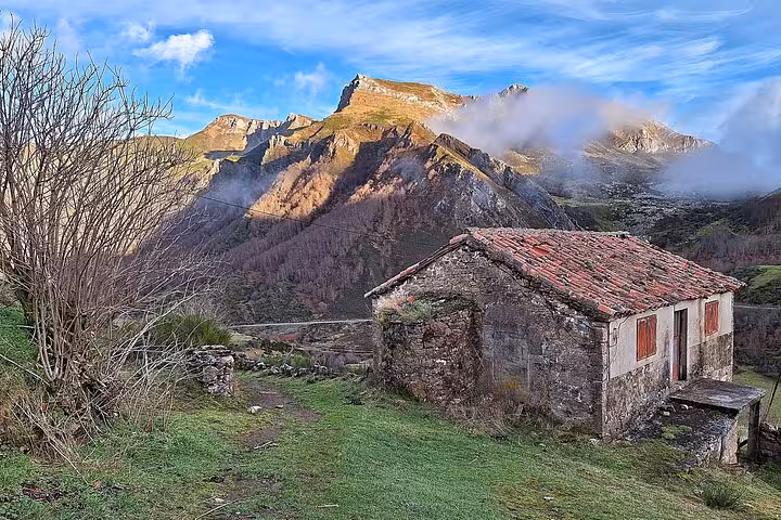 Rustic stone cottage in Somiedo Natural Park with misty mountains and lush greenery, perfect for guided village tours.