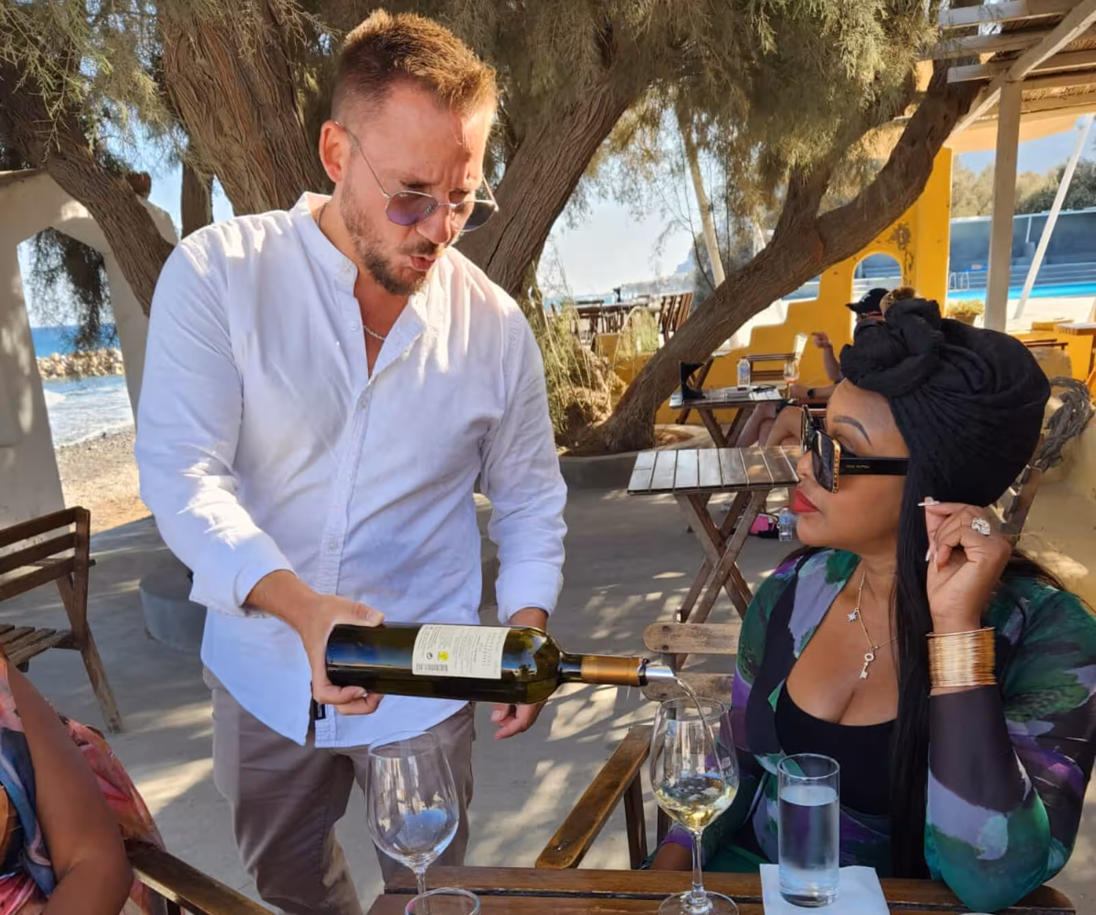 Sommelier pours Santorini white wine at seaside taverna during private day or sunset wine tasting tour