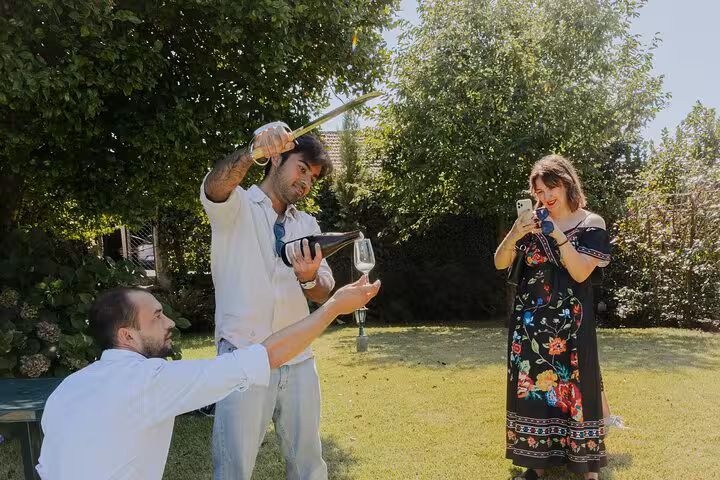 Sommelier sabers sparkling wine as guests film in a sunny Douro Valley winery garden near Porto during a wine tasting tour