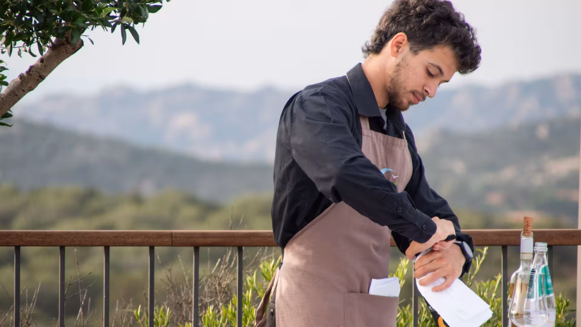 Sommelier uncorking a wine bottle at a Gallura winery with stunning mountain views.