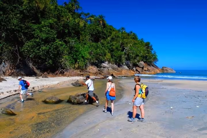 Adventurers explore a pristine beach with lush greenery and clear blue skies at Sono Beach, perfect for hiking and relaxation.