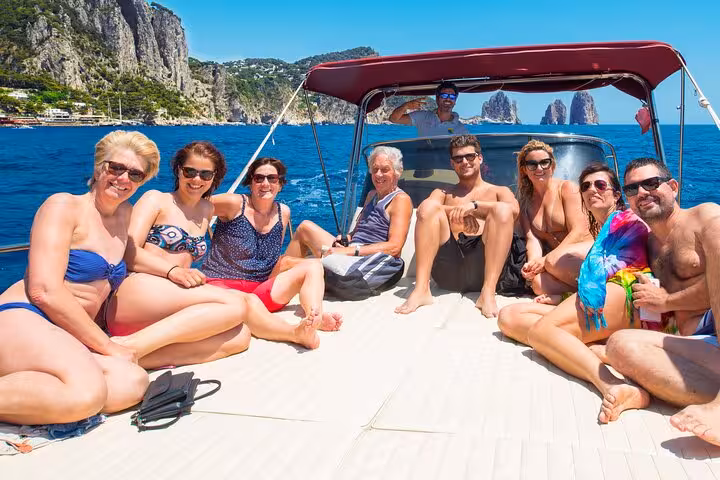Group enjoying a sunny day on a classic Gozzo boat tour from Sorrento to Capri, with stunning Faraglioni rocks in the background.