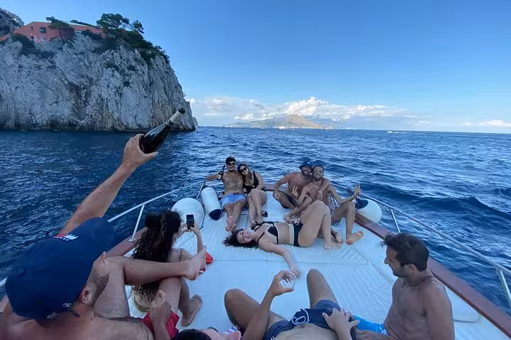 Group enjoying a sunny boat tour along Sorrento Coast with stunning cliffs and clear blue waters.
