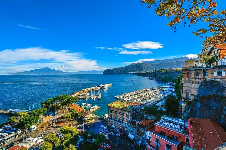Stunning view of Sorrento's coastline with a marina, vibrant blue sea, and distant mountains under a clear sky.