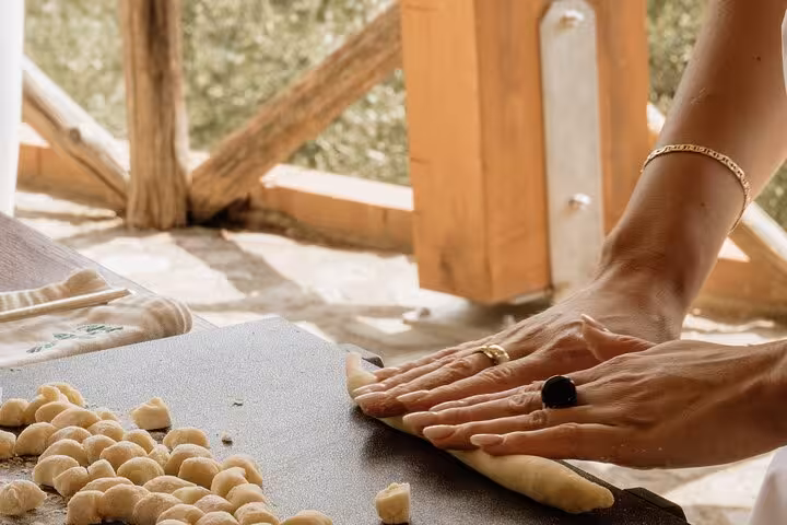 Hands rolling dough for gnocchi on a wooden table during a Sorrento cooking class with scenic views.