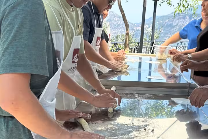 Participants shaping dough during a scenic Sorrento cooking class with a local chef, overlooking the stunning coastline.