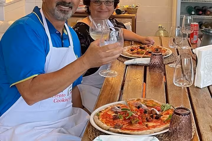Couple enjoying homemade pizza and wine at a rustic table during a Sorrento cooking class lunch.