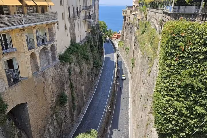 Scenic view of a narrow street in Sorrento flanked by cliffs, leading to the azure sea, perfect for a guided walking tour.