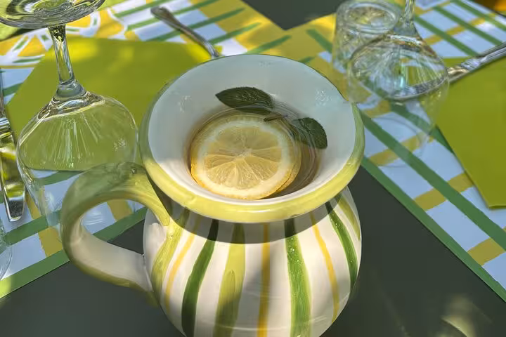 A decorative jug filled with fresh lemon water and mint leaves, set on a colorful table in a Sorrento lemon grove.