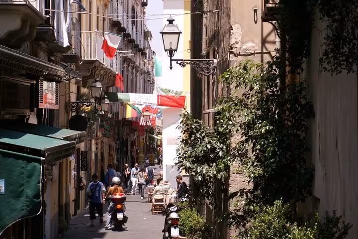 Charming narrow street in Sorrento with colorful flags, scooters, and pedestrians, capturing vibrant Italian culture.
