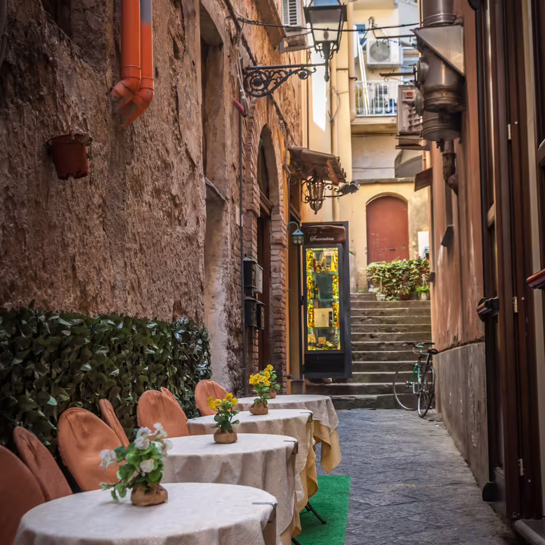 Charming narrow alley with outdoor café tables and flowers in old town Sorrento, a highlight of the trekking weekend tour