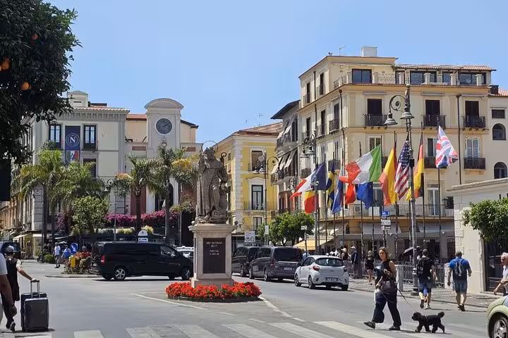 Bustling Sorrento square with vibrant buildings, flags, and a statue, capturing the essence of a walking tour adventure.