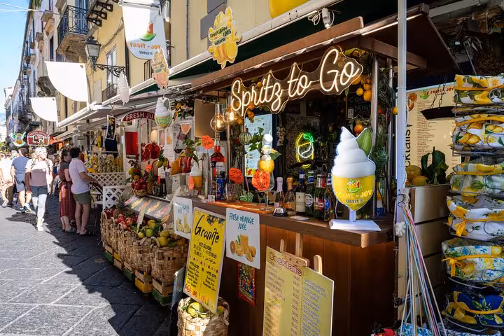 Bustling Sorrento street market with vibrant fruit stands and Spritz to Go bar on a sunny day.