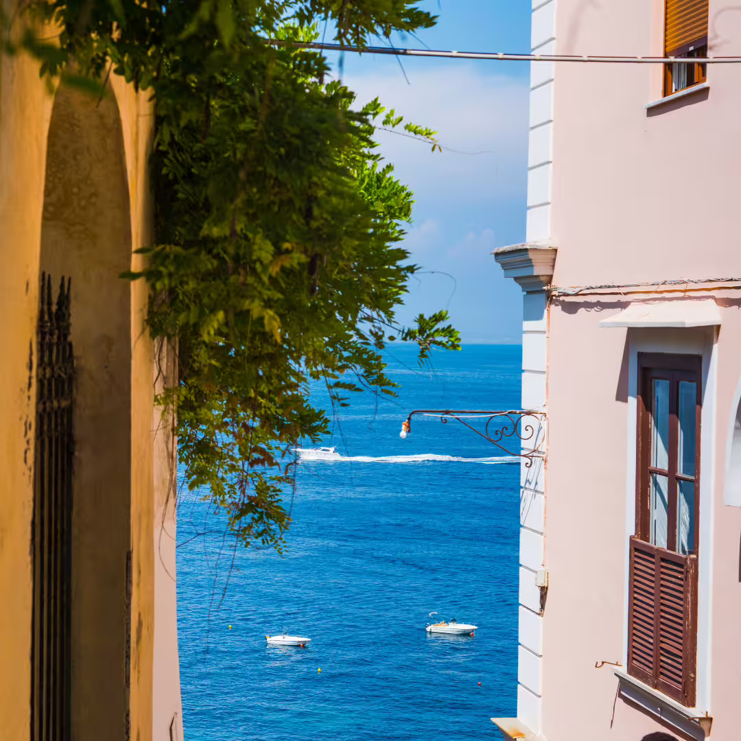 View of the blue Tyrrhenian Sea from a Sorrento lane between pastel houses, boats and coastal trekking route below