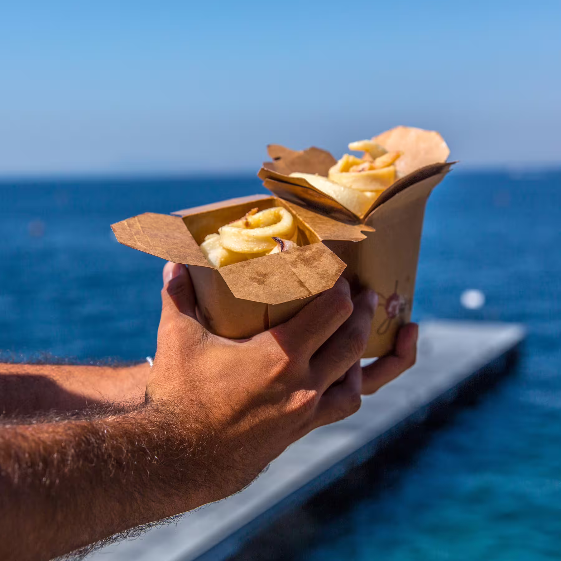 Hands holding cones of fresh Italian street food by the blue sea, part of Sorrento's guided walking tour.