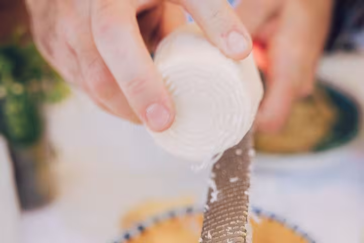 Hand grating cheese over a dish, showcasing culinary preparations for the Sorrento wine pairing tour.