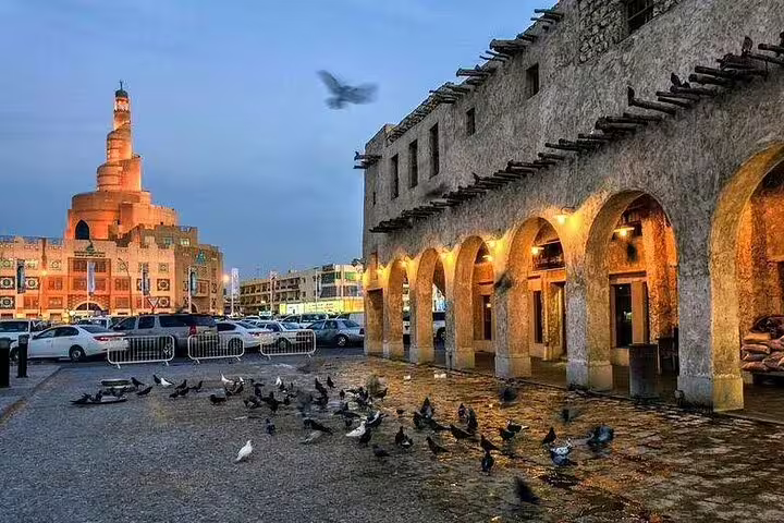 Pigeons in front of Souq Waqif with the illuminated spiral mosque in Doha, Qatar during a city tour.