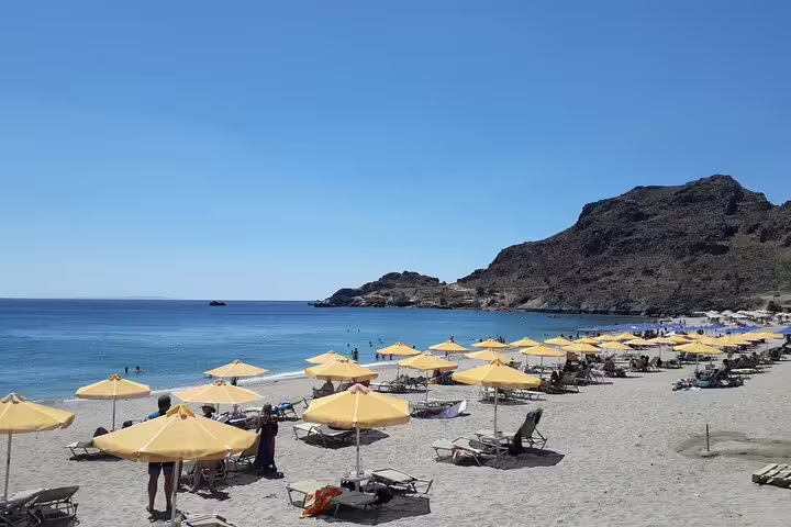 Pristine sandy beach with yellow umbrellas and clear blue waters on the South Coast of Crete, perfect for relaxation on a private tour.