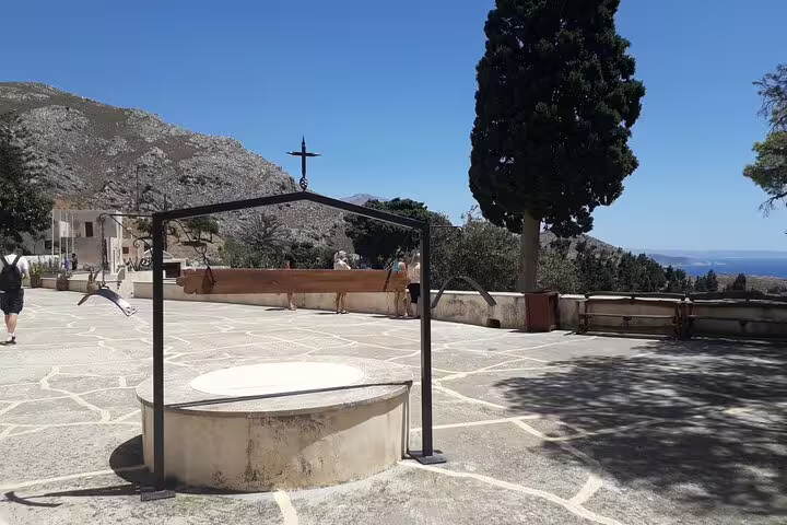 Scenic courtyard view on the South Coast of Crete with distant mountains and a cross under a clear blue sky.