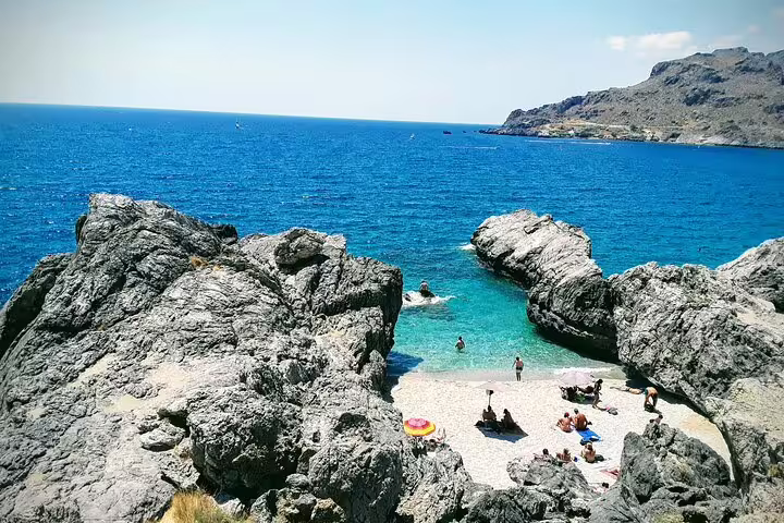 Tourists relaxing on a secluded rocky beach with turquoise waters on the South Coast of Crete.