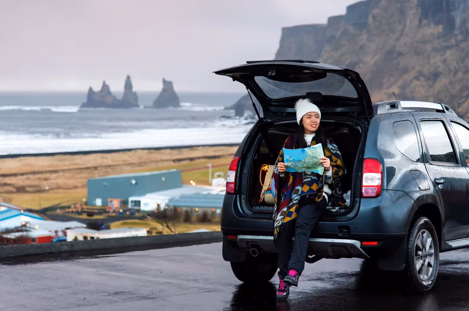 Traveler with map enjoying scenic view from car near Reynisdrangar sea stacks in South Iceland.