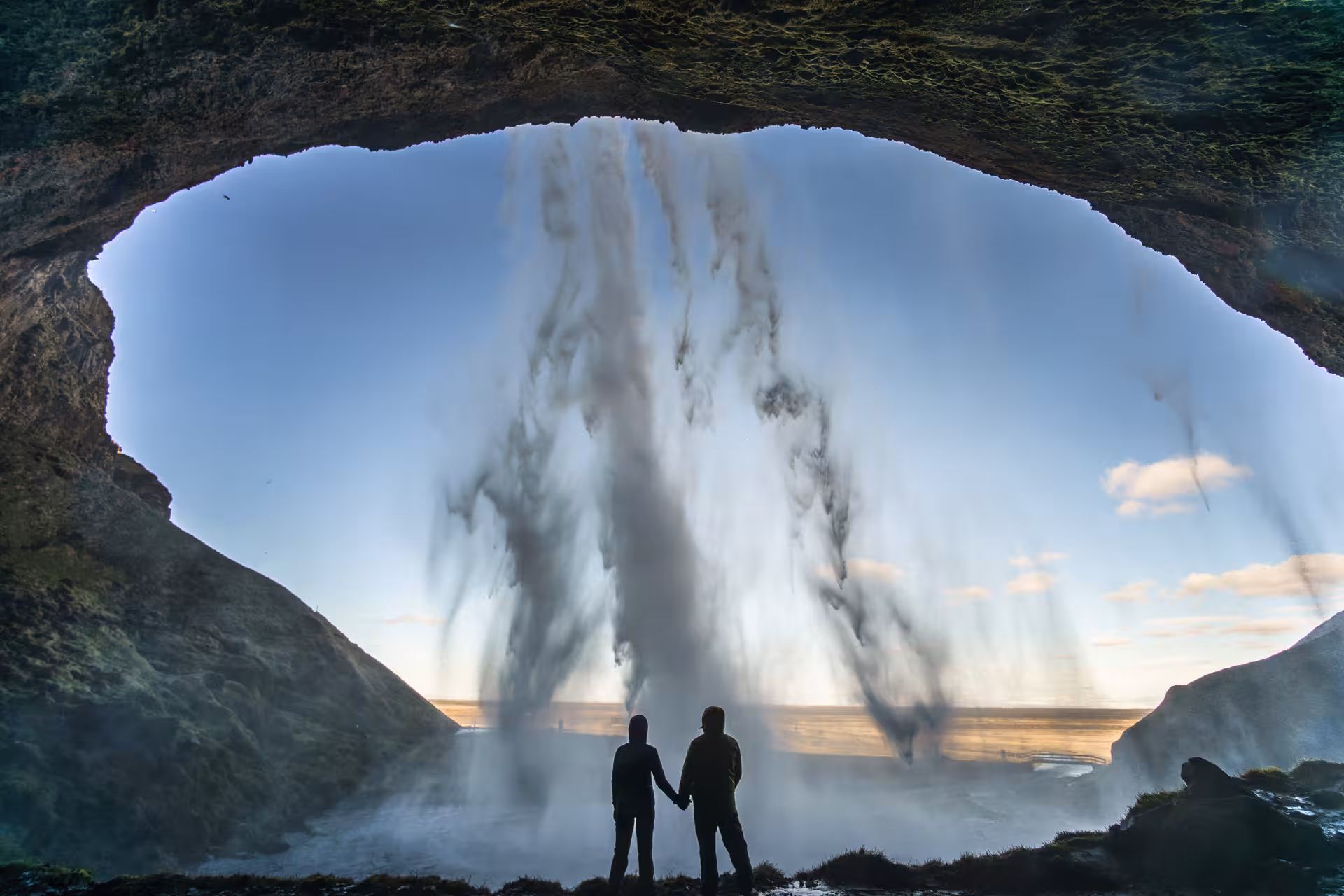 Two people holding hands behind a majestic waterfall, experiencing the South Shore's breathtaking natural beauty.