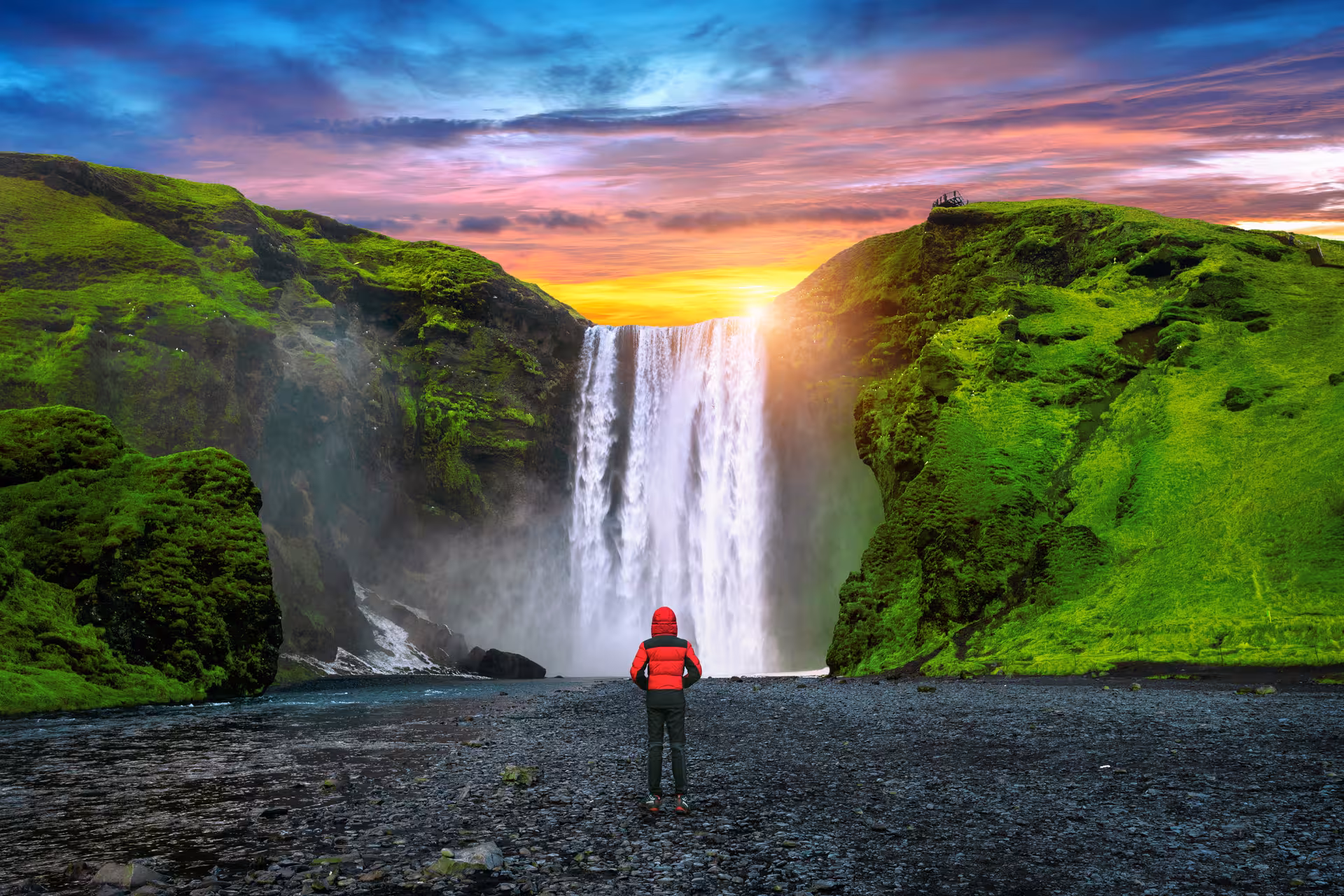 Traveler in red jacket gazing at a stunning waterfall with vibrant sunset sky on the South Shore adventure tour.