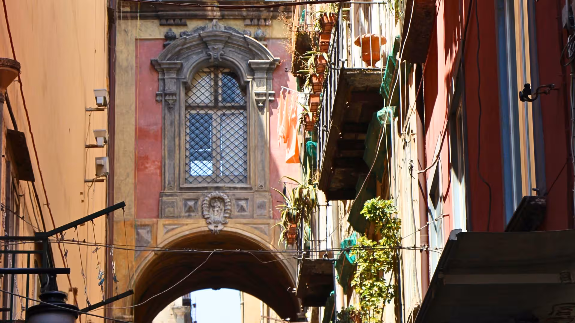 Charming narrow alley in Spaccanapoli, Naples, with colorful buildings and hanging plants.